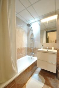 Baño con lavabo con mueble blanco denajo y espejo encima; y bañera con cortina.