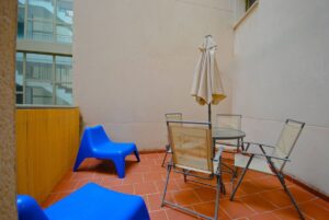Terraza con mesa redonda con sombrilla y 4 sillas; y dos sillones de plástico azules.