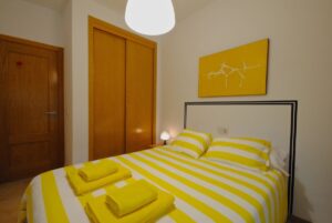 Dormitorio con cama doble decorada con cojines y toallas, mesita de noche, y armario empotrado.