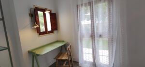 Sala con escritorio con silla bajo ventana, y puerta de salida a terraza.