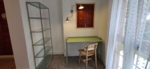 Sala con estantería, escritorio con silla y puerta de salida a terraza.